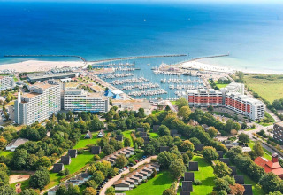 Luchtzicht op een jachthaven met boten, hotels en groene hutten aan zee op een zonnige dag.