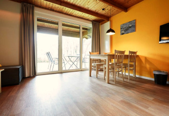 Bright lodge living room with wooden ceiling, yellow wall, dining table, and terrace view through glass doors.