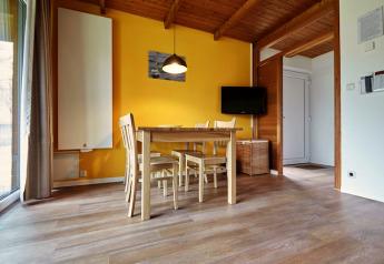 Bright lodge dining area with wooden floor, yellow wall, dining table, four chairs, and a flat TV.