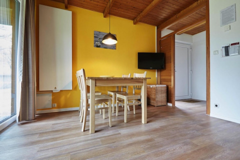 Sala da pranzo luminosa in un lodge con pavimento in legno, parete gialla, tavolo, quattro sedie e TV.