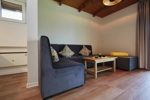 Gezellige lodge woonkamer met grijze hoekzetel, houten salontafel en sierkussens met motief.