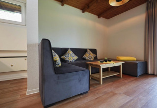 Sala moderna en una cabaña, con sofá gris en esquina, mesa de madera y cojines decorativos.