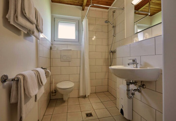 Lodge bathroom featuring a toilet, sink, walk-in shower with curtain, white towels, and tiled walls.
