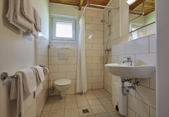 Badezimmer einer Lodge mit WC, Waschbecken, Dusche, weißen Handtüchern und hellen Fliesen an den Wänden.