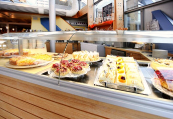 Una variedad de pasteles frescos y tartas se exhiben tras un vidrio en una acogedora cafetería de montaña.