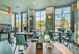Interior de lodge moderno con grandes ventanales, sillas verdes elegantes y luz natural acogedora.