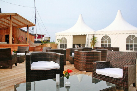 Zona lounge al aire libre en un lodge con sillones de mimbre, piso de madera y toldos blancos al fondo.