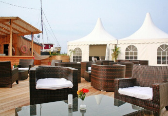 Buitenlounge van een lodge met rotan stoelen, houten terras en witte tenten in de achtergrond.