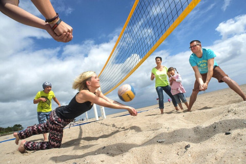 Famiglia che si diverte giocando a beach volley su una spiaggia sabbiosa vicino a un lodge sotto il cielo nuvoloso.