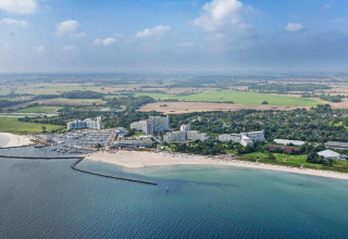 Vista aérea de una zona de cabañas costeras con playa, puerto deportivo, hoteles y campos bajo cielo nublado.