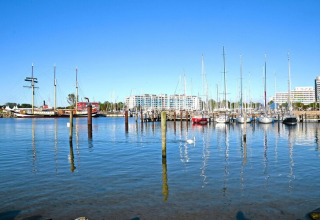 Vista de un puerto deportivo con veleros, barco histórico y edificios de una posada bajo cielo despejado.