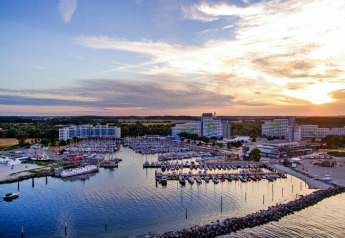 Blick auf einen Yachthafen mit Booten und großen Hotelgebäuden bei Sonnenuntergang, umgeben von Natur.