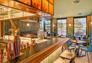 Moderne bar met houten toog en groene stoelen bij Blockhouse HiPr 4 Pers in Duitsland, grote ramen zichtbaar.