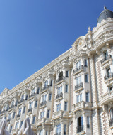 Majestuoso edificio histórico con balcones detallados y palmeras, destacado bajo un cielo azul en la Costa Azul.