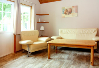Bright living area with cream sofa, armchair, wood floor and table at Holiday park Markgrafenheide Warnemünde.