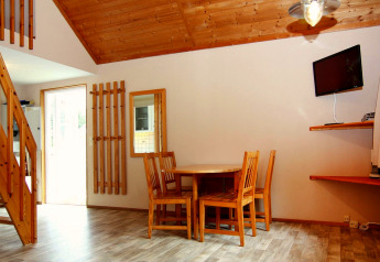 Gemütlicher Innenraum in einer Ferienwohnung mit Esstisch, Holzstühlen, Treppe und Wand-TV.