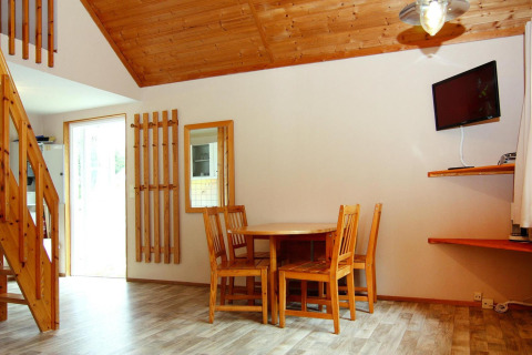 Cozy lodge interior with wooden dining set, staircase, wall-mounted TV, large window, and wood ceiling.