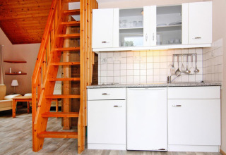 Modern lodge kitchen with white cabinets and a wooden staircase at Holiday Park Markgrafenheide Warnemünde, Germany.