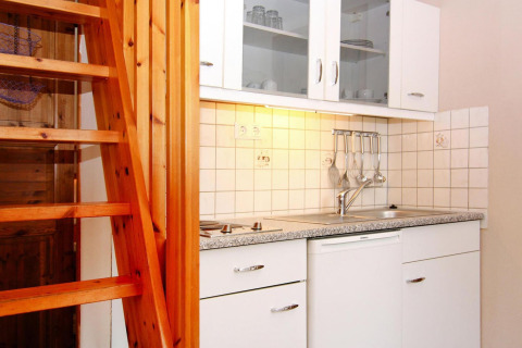 Compacte kitchenette met witte kasten, houten trap en keukengerei in Markgrafenheide, Duitsland.