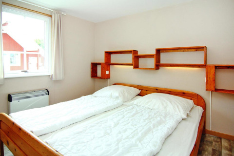Bedroom with double bed and wooden shelving on the wall in Holiday park Markgrafenheide Warnemünde, Germany.