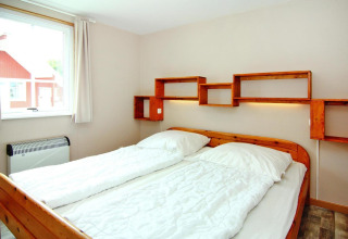 Bedroom with double bed and wooden shelving on the wall in Holiday park Markgrafenheide Warnemünde, Germany.