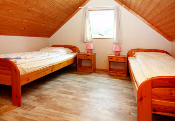 Room with two single beds, wooden floor and sloped ceiling at Holiday park Markgrafenheide Warnemünde, Germany.