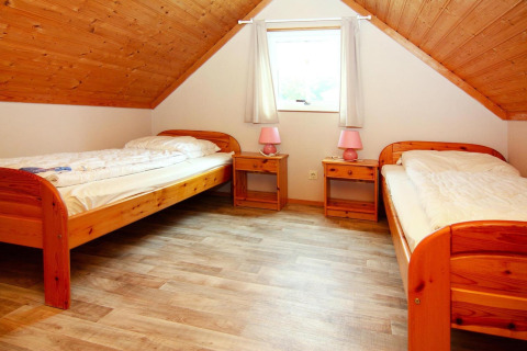Habitación con dos camas individuales, suelo de madera y techo inclinado en Holiday park Markgrafenheide Warnemünde, Alemania.