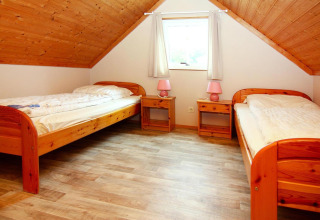 Habitación con dos camas individuales, suelo de madera y techo inclinado en Holiday park Markgrafenheide Warnemünde, Alemania.