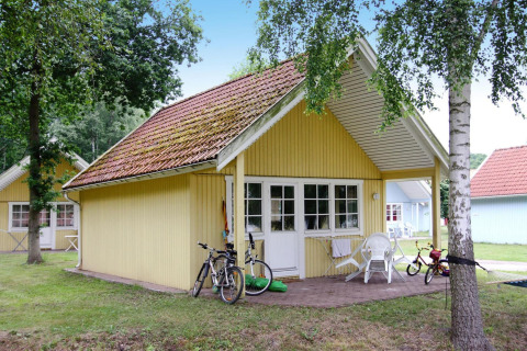 Geel houten huis met veranda, fietsen en kinderspeelgoed in vakantiepark Markgrafenheide Warnemünde, Duitsland.