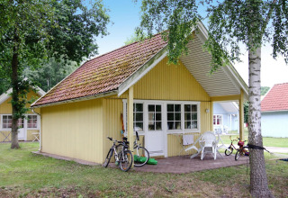 Yellow wooden lodge with porch, bikes, and children's toys at Holiday Park Markgrafenheide Warnemünde, Germany.