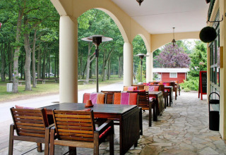 Covered outdoor terrace with wooden tables and colorful chairs at Holiday park Markgrafenheide Warnemünde, Germany.