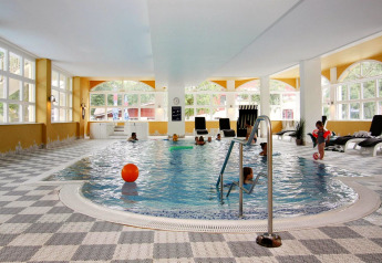 Piscina coperta con bambini, lettini e grandi finestre presso l'Holiday Park Markgrafenheide Warnemünde.