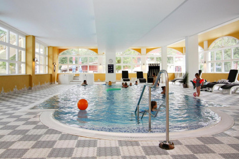 Indoor swimming pool with children, lounge chairs, and large windows at Holiday Park Markgrafenheide Warnemünde.