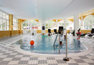 Indoor swimming pool with children, lounge chairs, and large windows at Holiday Park Markgrafenheide Warnemünde.