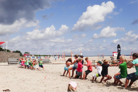 Niños juegan a la cuerda en la playa arenosa bajo nubes en Blockhouse HiPr 4 Pers en Alemania.
