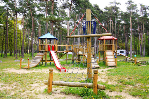 Wooden playground with a slide and climbing net in a forest at Holiday park Markgrafenheide Warnemünde, Germany.