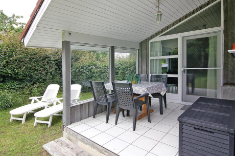 Overdækket terrasse med spisebord, stole og liggestole i grøn have ved Holiday home i Hünning, Tyskland.