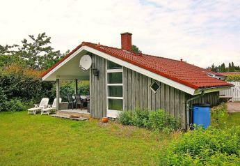 Charmante maison de vacances à Hünning, Allemagne, avec toit rouge, terrasse couverte et jardin vert.