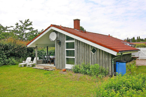 Acogedora casa de vacaciones en Hünning, Alemania, con techo rojo, porche y jardín verde exuberante.