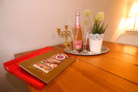 Tavolo accogliente al Holiday home «in Hünning», Germania, con spumante, bicchieri, pianta e portacandele.