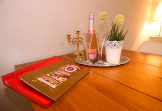 Tavolo accogliente al Holiday home «in Hünning», Germania, con spumante, bicchieri, pianta e portacandele.