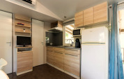 Cocina moderna de mobil home en Camping del Mar, España, con armarios de madera, nevera y microondas.