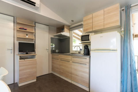 Cuisine de mobil-home moderne au Camping del Mar en Espagne, avec placards bois, frigo et micro-ondes.