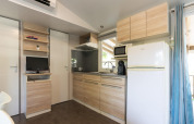 Cocina moderna de mobil home en Camping del Mar, España, con armarios de madera, nevera y microondas.