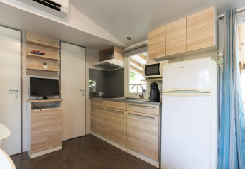 Cocina moderna de mobil home en Camping del Mar, España, con armarios de madera, nevera y microondas.