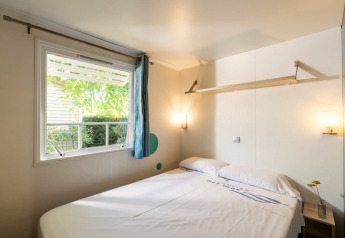 Slaapkamer in Camping del Mar MOBILE HOME 6P in Spanje met tweepersoonsbed, groot raam en eenvoudige inrichting.