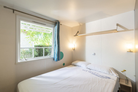 Chambre du Camping del Mar MOBILE HOME 6P en Espagne avec lit double, grande fenêtre et déco simple.