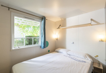 Dormitorio en Camping del Mar MOBILE HOME 6P en España con cama doble, ventana amplia y decoración sencilla.