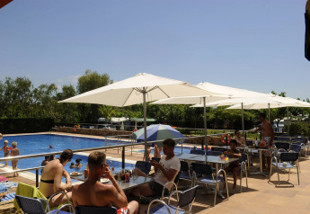 Glamping-Unterkunft mit Pool, Menschen entspannen unter Sonnenschirmen, Kinder spielen im Wasser.