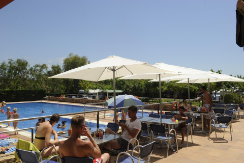 Alojamiento glamping con piscina, gente relajándose bajo sombrillas y niños jugando en el agua.